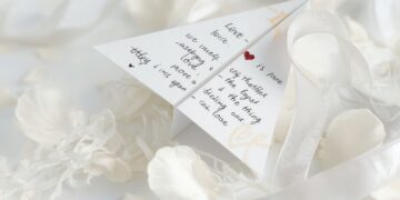 Papierflieger mit Liebesbotschaft auf weißem Tisch mit Rosenblüten zur Hochzeit