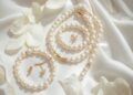 Klassischer Brautperlenschmuck – Perlenkette, Ohrstecker und Armband auf weißem Satin