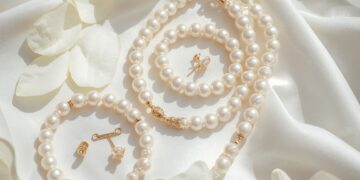 Klassischer Brautperlenschmuck – Perlenkette, Ohrstecker und Armband auf weißem Satin